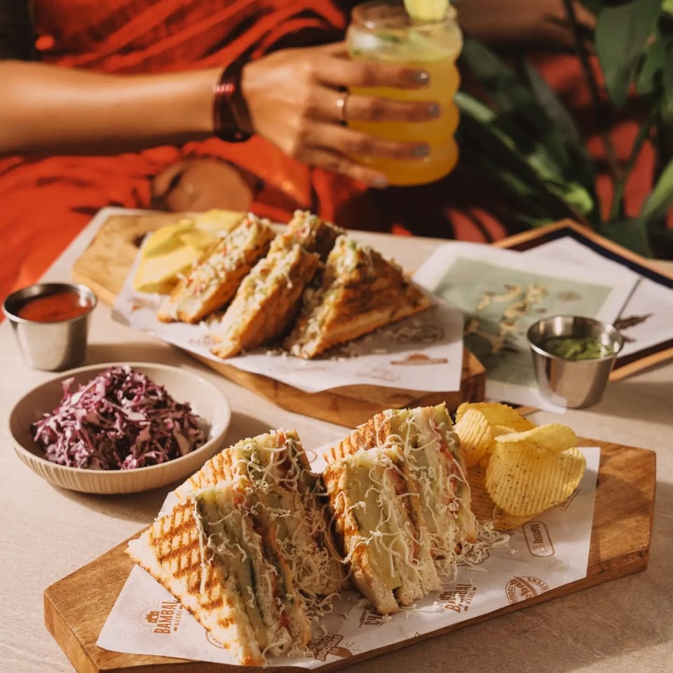 Grilled sandwiches with shredded cheese, ridged chips, slaw, dipping sauces, and a citrus cocktail on a restaurant table.